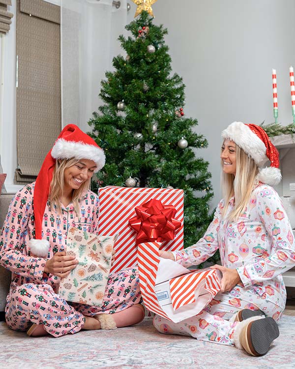 two girls wrapping presents in front of a christmas tree