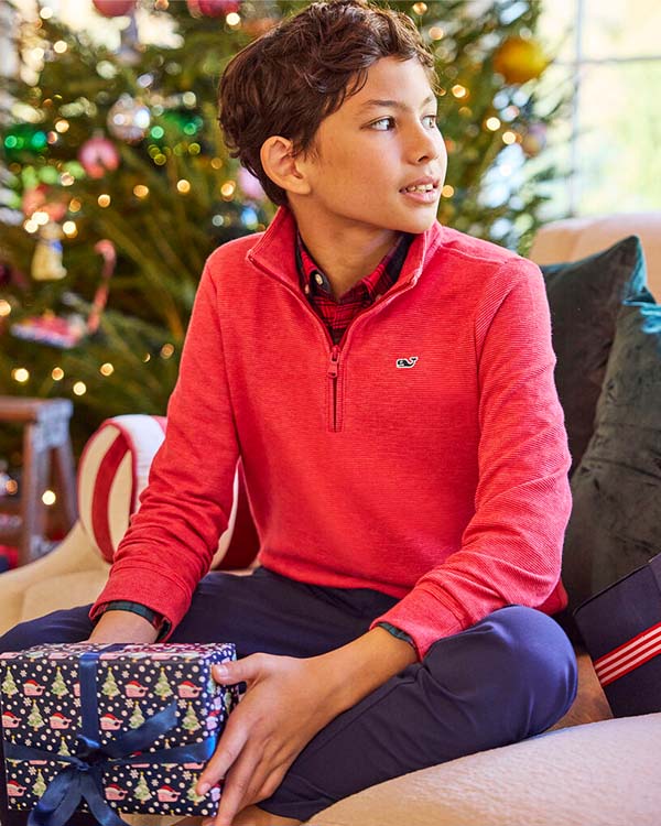 young boy sitting in front of a christmas tree holding a present
